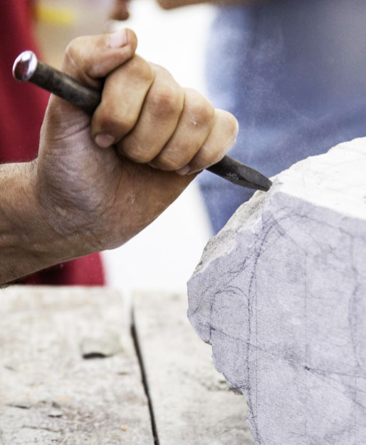 A sculptor skillfully uses a chisel to shape a marble statue indoors, showcasing artistry and craftsmanship.